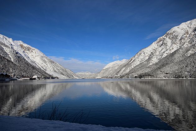 Die winterlichen Berge spiegeln sich bei Sonnenschein im Achensee.